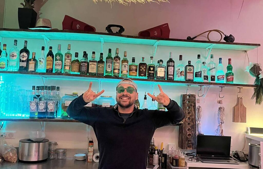 Barman derrière son comptoir avec une casquette et des lunettes.