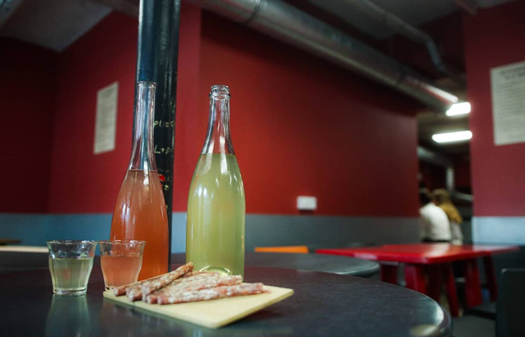 Deux bouteilles de jus, des saucissons sur une planche et un verre remplis.